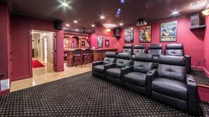 Ein Heimkinozimmer mit einer schwarzen Ledersofa, einer Bar und roten Wänden.