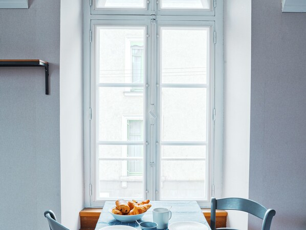 Ein Esstisch mit einer Schüssel Croissants und einer Tasse vor einem Fenster mit Blick auf Gebäude.