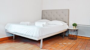 A neatly made bed with white linens, a tufted headboard, and a small bedside table with a plant. - Le Woody - Proche Gare - Télétravail (Laval)