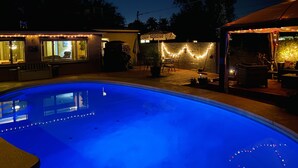 A swimming pool with a blue tint, surrounded by outdoor seating and string lights. - Central location with all the right amenities for the perfect vacation. (Tucson)