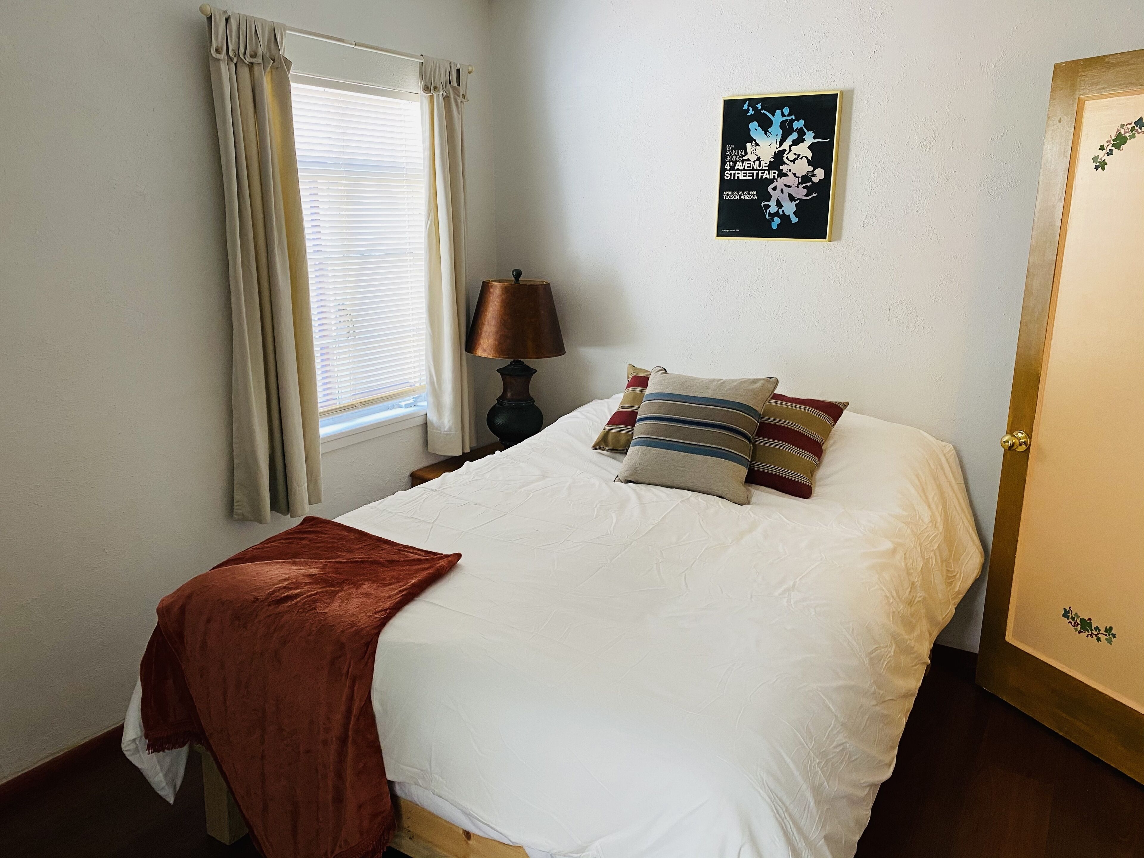 Een slaapkamer met een bed, een raam met gordijnen, een lamp en een ingelijste foto aan de muur.
