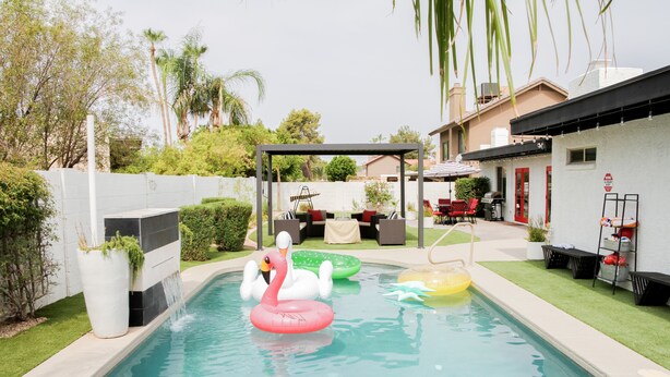 Une piscine avec des bouées en forme de cygne gonflables, un patio couvert et un mur extérieur blanc.