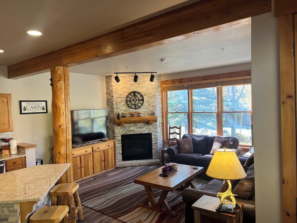 A cabin interior with a stone fireplace, a television, a sofa, and a dining area. - Shuttle to Slopes, Private Entrance, Hot Tub Access, Private Patio with Grill (Keystone)