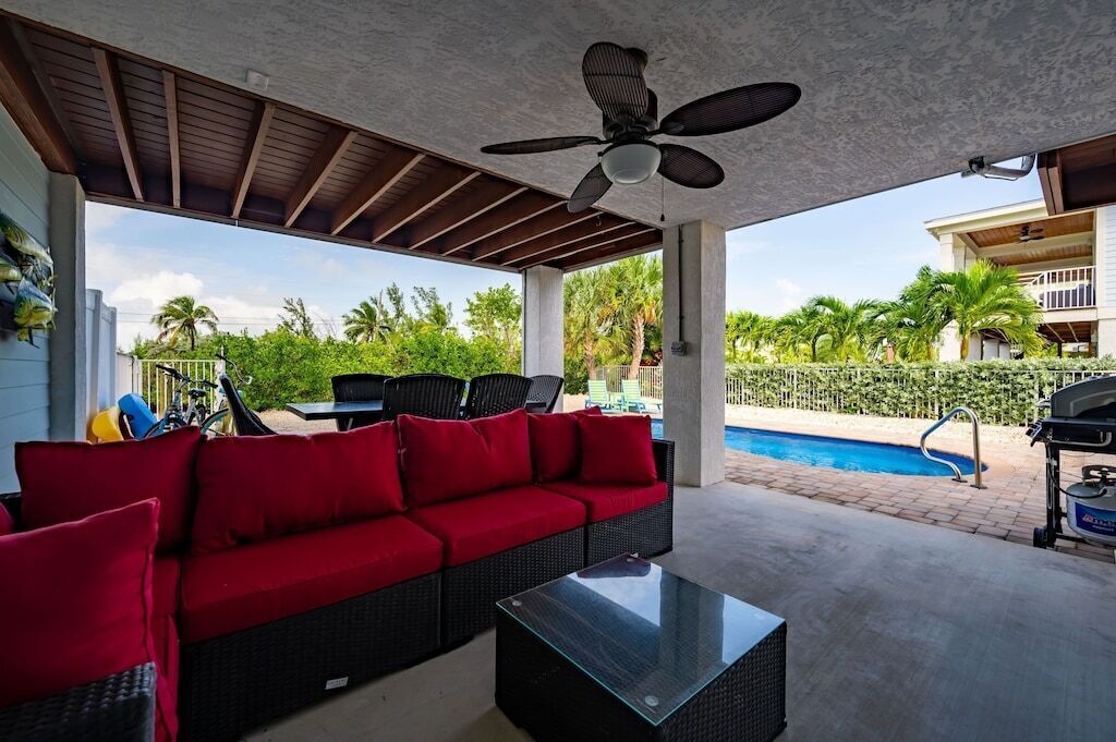Une terrasse extérieure avec un canapé rouge, une table en verre et un ventilateur de plafond.