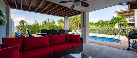 An outdoor patio with a red sofa, a glass table, and a ceiling fan.