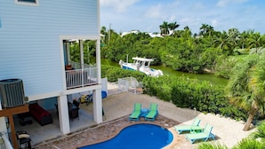 A swimming pool with lounge chairs, a covered deck, and a view of a boat on a waterway. - Canal-Front Oasis with Pool & Dock (Marathon)