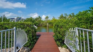 A wooden pathway leading to a body of water, surrounded by lush greenery and palm trees. - Canal-Front Oasis with Pool & Dock (Marathon)