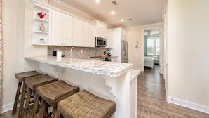A kitchen with white cabinets, a granite countertop, and wooden stools. - Canal-Front Oasis with Pool & Dock (Marathon)