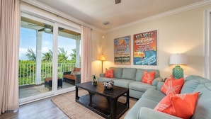 A living room with a sofa, coffee table, and a view of the outdoors. There are two posters on the wall and a lamp on the side table. - Canal-Front Oasis with Pool & Dock (Marathon)