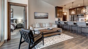 A modern living room with a sofa, coffee table, and chairs, a kitchen with a refrigerator and microwave, and a dining area with bar stools. - Modern Mountain Luxury - Bonus room, Humidifier, Wi-Fi & Hot Tub! (Kamas)