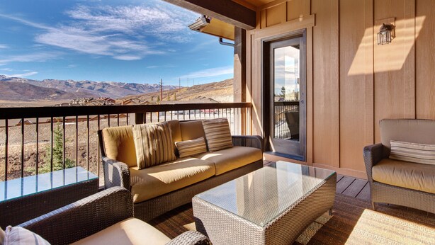 A balcony with wicker furniture, a glass table, and a view of mountains. - Modern Mountain Luxury - Bonus room, Humidifier, Wi-Fi & Hot Tub! (Kamas)