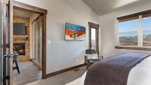 A bedroom with a fireplace, a large window with a mountain view, and a painting on the wall. - Modern Mountain Luxury - Bonus room, Humidifier, Wi-Fi & Hot Tub! (Kamas)