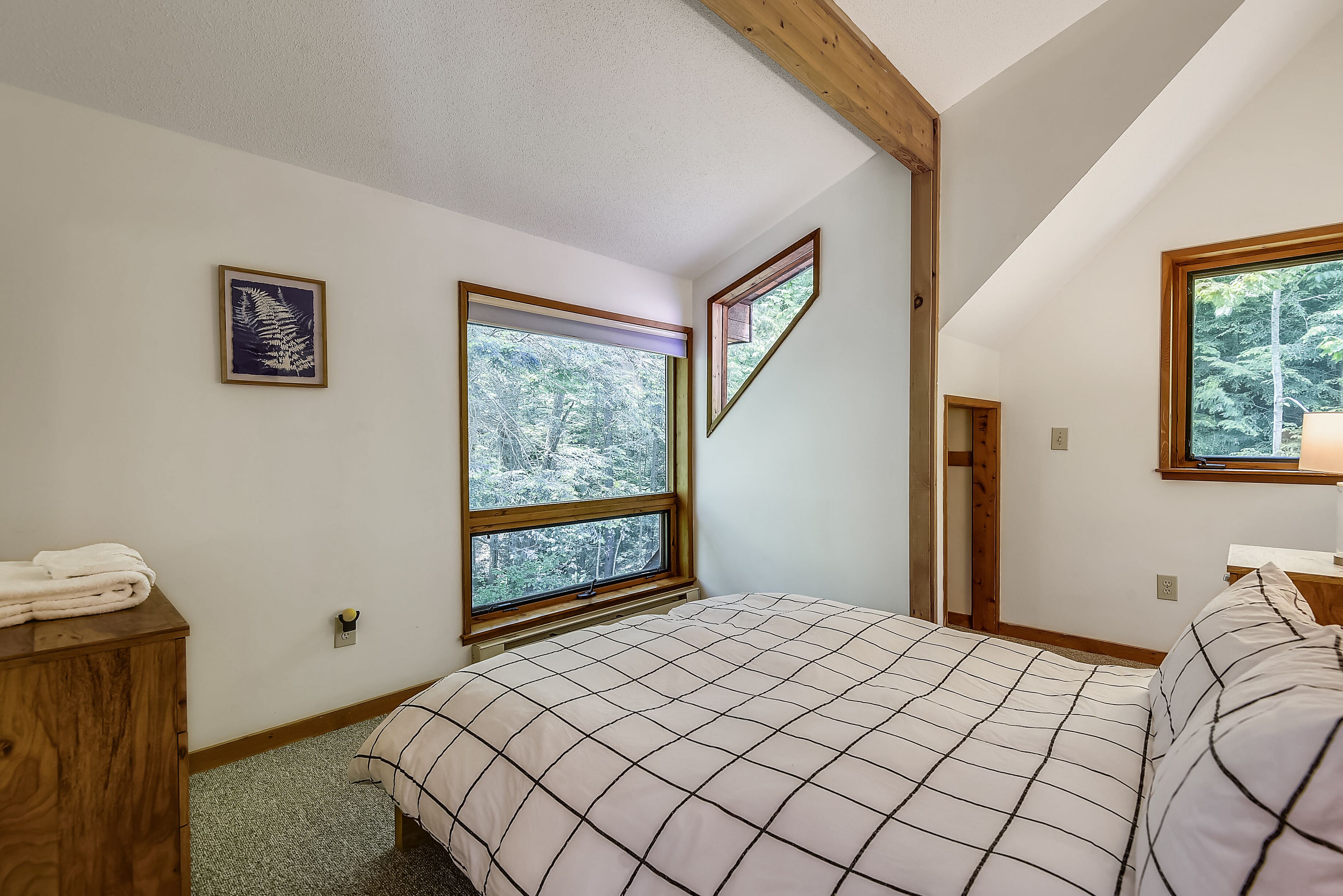Una camera da letto con un letto grande, due finestre, una testiera in legno e un piccolo comò di legno.