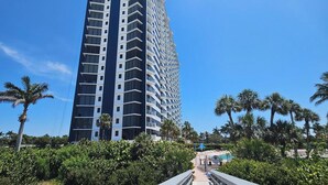 A tall, modern hotel with a straight facade and balconies, surrounded by palm trees and a wooden boardwalk. - Sunny Oceanfront Condominium, Short Walk to the Beach (Marco Island)