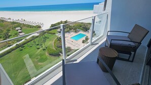 A balcony with a view of a beach, a pool, and a lush garden. - Sunny Oceanfront Condominium, Short Walk to the Beach (Marco Island)