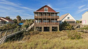 Ein zweistöckiges Holzhaus mit einem Balkon, umgeben von einer Holzterrasse und einer Rasenfläche.