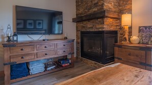 Ein Wohnzimmer mit Kamin aus Stein, einem Flachbildfernseher, Holzmöbeln und einem Teppich.