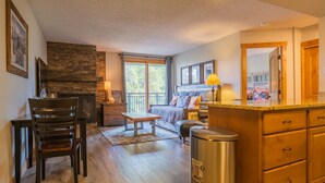 Ein gemütliches Wohnzimmer mit Kamin, ein Essbereich mit Holztisch und -stühlen, eine Küche mit Holzschränken und ein Balkon mit Blick auf Bäume.