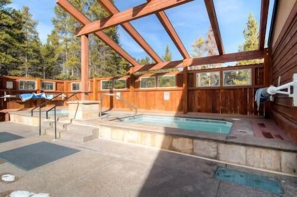 Una cabaña de madera con jacuzzi y piscina, rodeada de árboles.