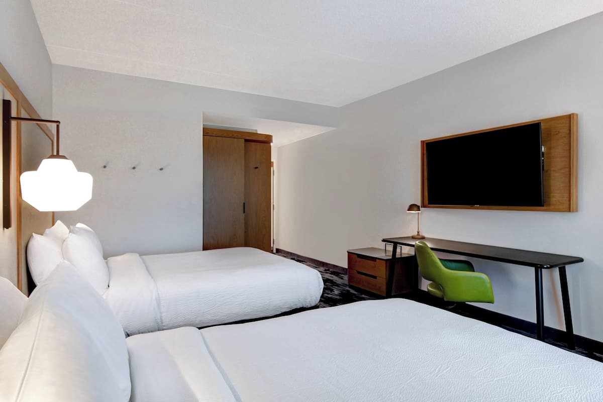 Ein Hotelzimmer mit zwei Betten, einem Schreibtisch, einem Sessel, einem Fernseher und einer Lampe.