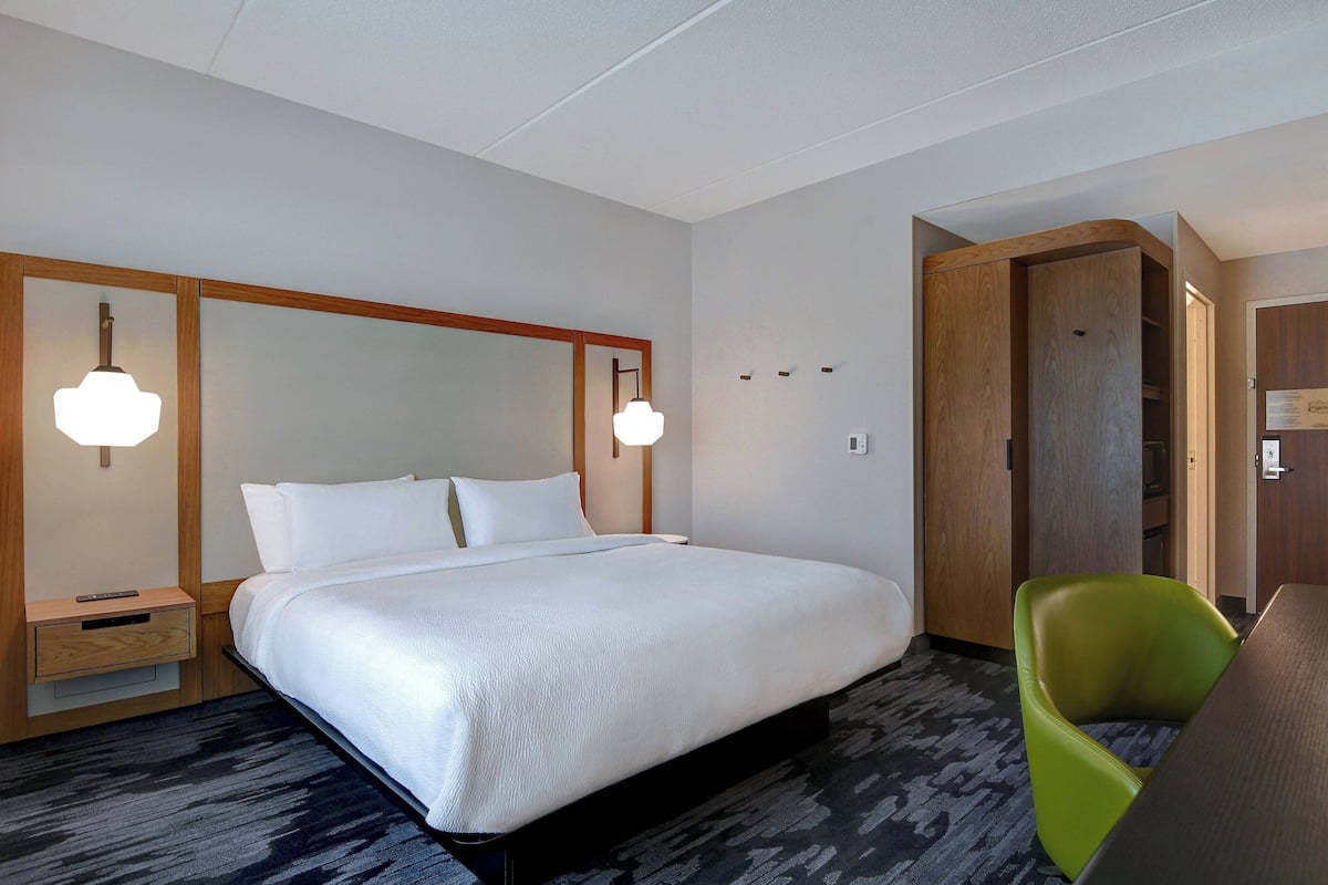 Ein Hotelzimmer mit einem großen Bett, zwei Nachttischlampen, einem Holzschrank, einem grünen Sessel und einem Schreibtisch.