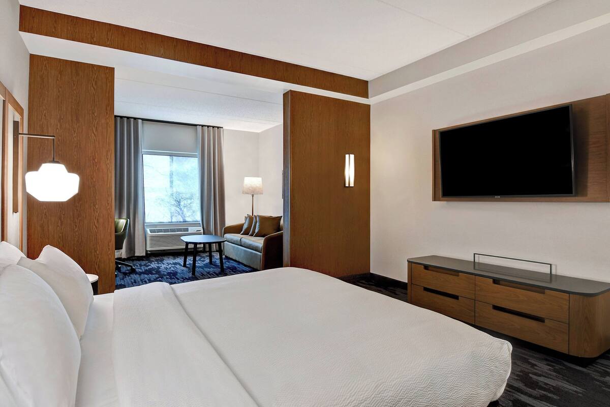 Ein Hotelzimmer mit einem großen Bett, einem an der Wand montierten Fernseher, einem Schreibtisch und einem Stuhl.