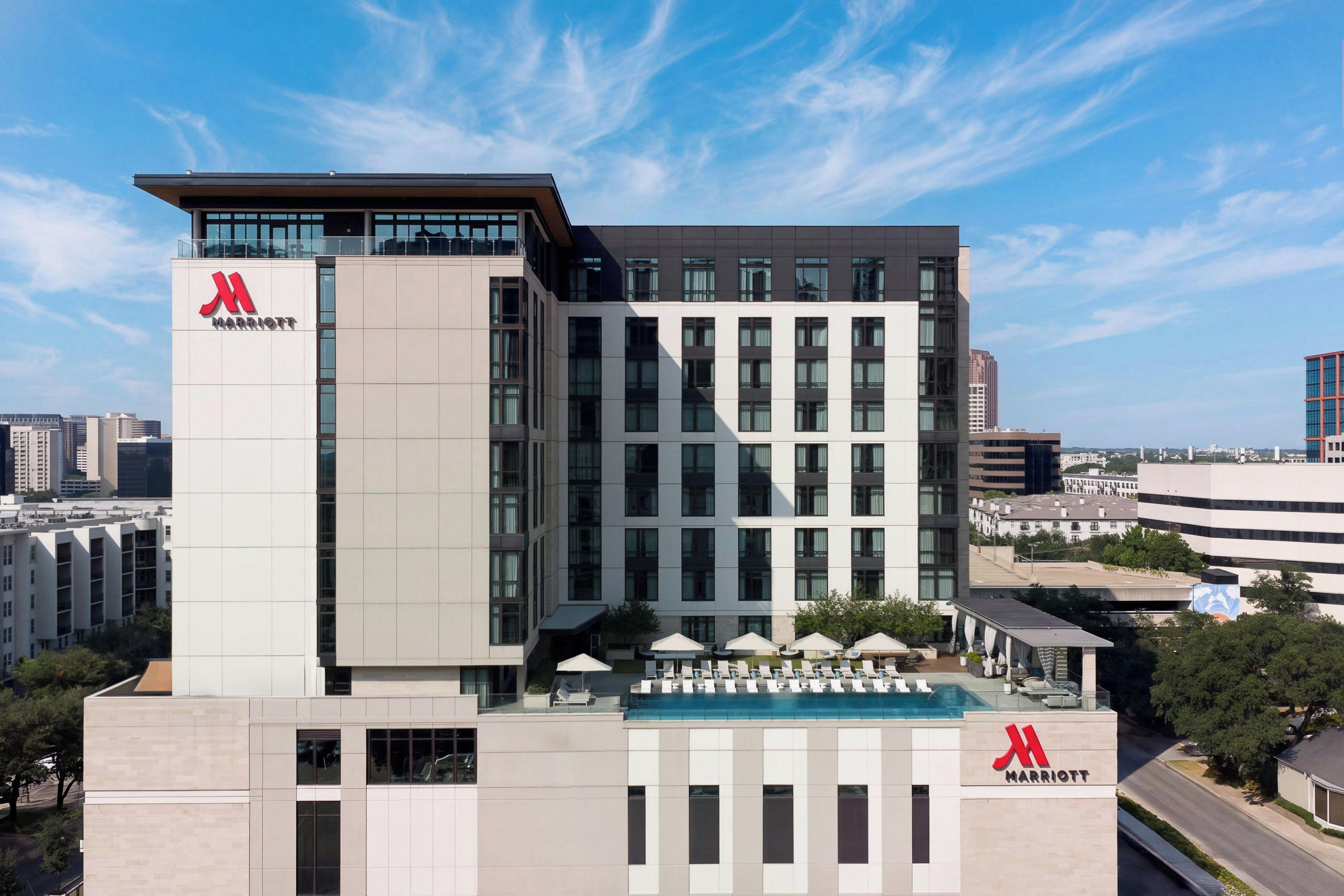 A modern hotel building with a prominent 'Marriott' logo, multiple floors, and a rooftop pool area.