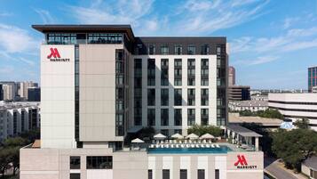 A modern hotel building with a prominent 'Marriott' logo, multiple floors, and a rooftop pool area.