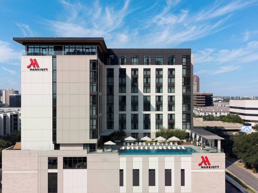 A modern hotel building with a prominent 'Marriott' logo, multiple floors, and a rooftop pool area.