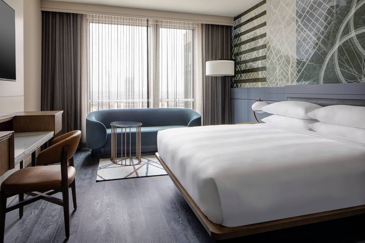 Ein modernes Hotelzimmer mit einem großen Bett, einem Schreibtisch, einem Sessel und einem blauen Sofa.