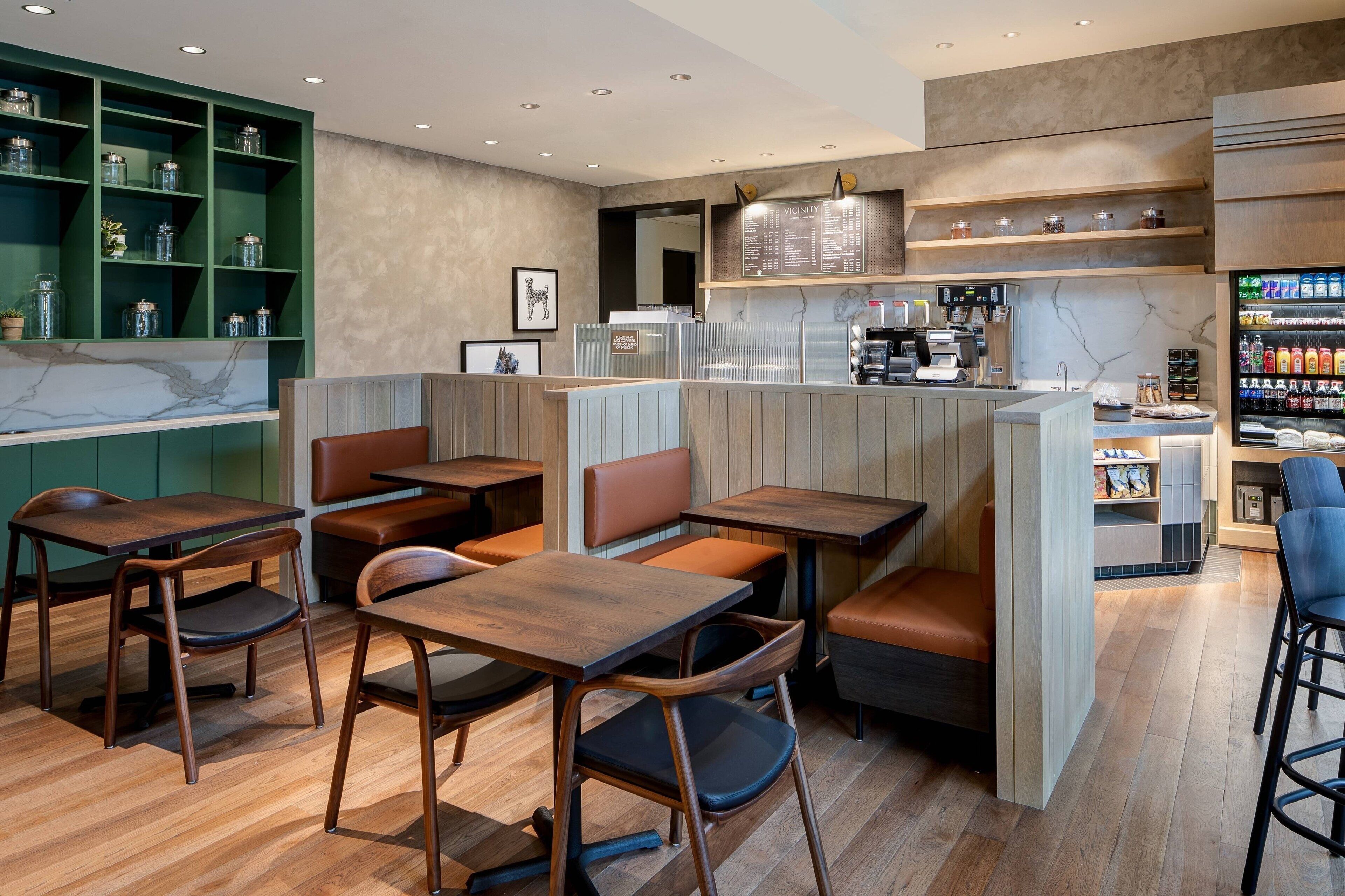 A modern cafe with wooden tables and booths, a coffee machine, and shelves with snacks.