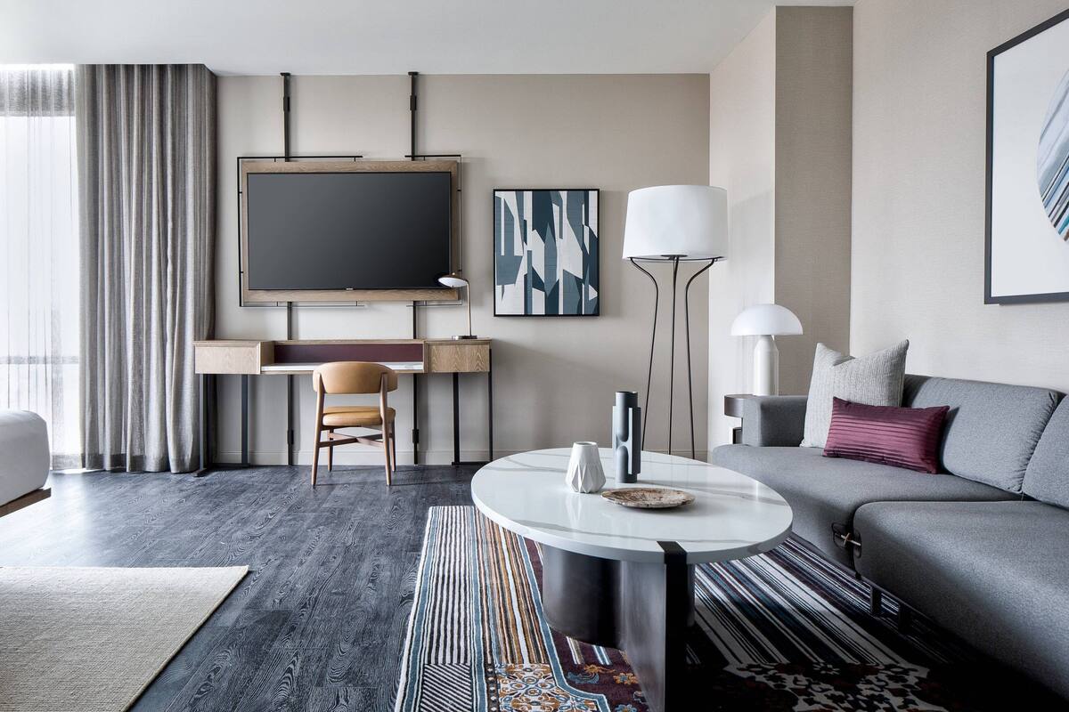 Ein modernes Hotelzimmer mit großem Flachbildfernseher, einer Couch, einem Esstisch und einem Schreibtisch mit Stuhl.