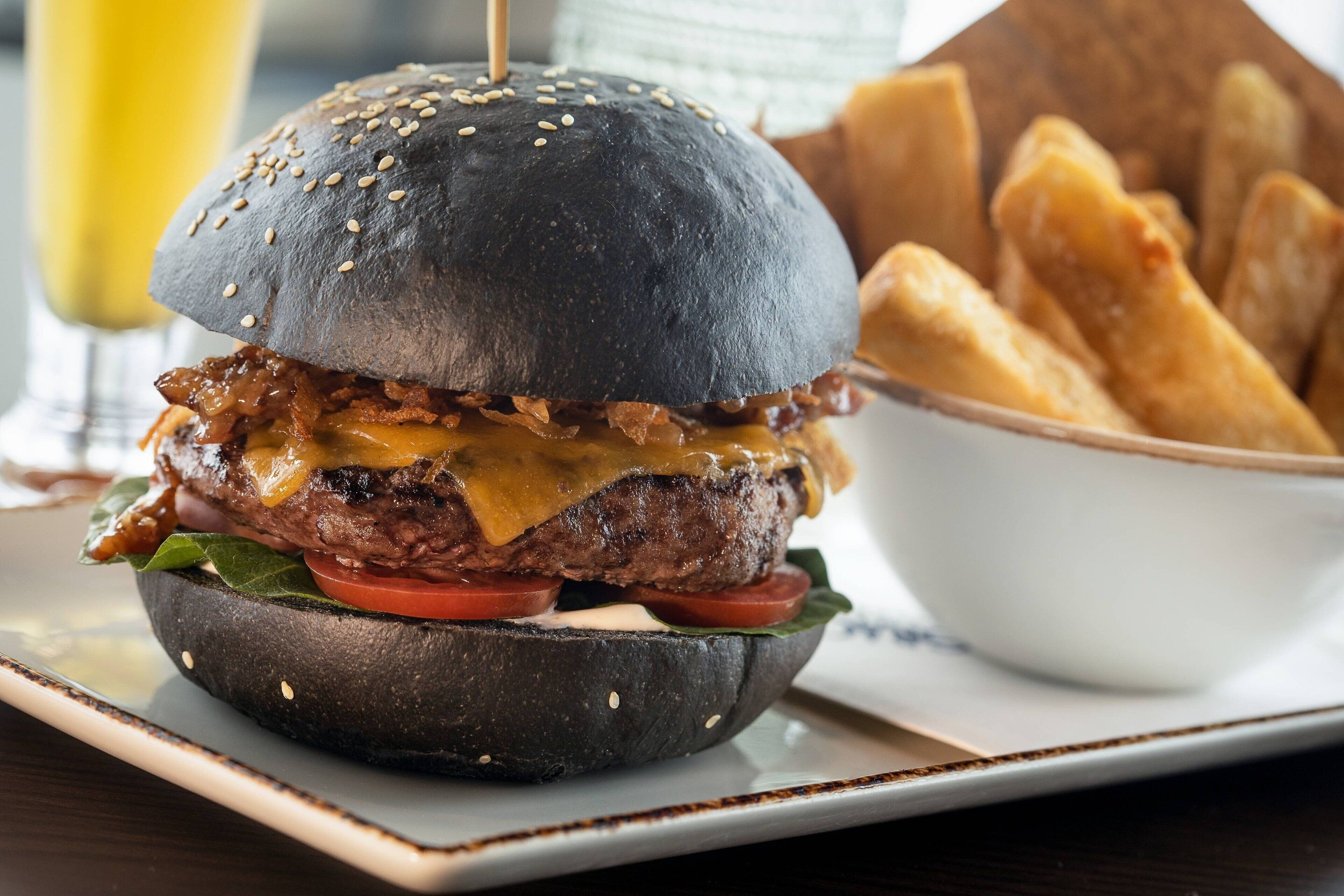 A burger with a sesame seed bun, cheese, lettuce, tomato, and bacon, served with fries.