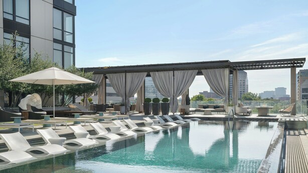 Una piscina en la azotea con sillones blancos y una pérgola con cortinas.