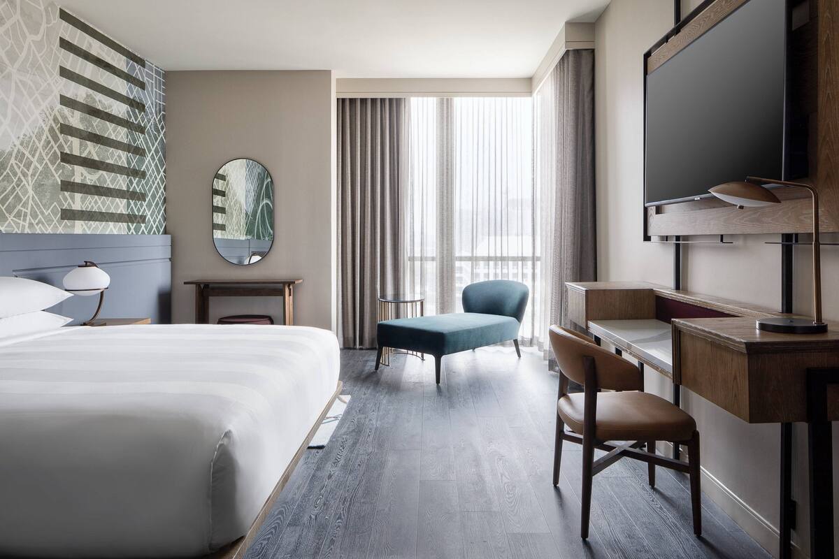 Ein Hotelzimmer mit einem großen Bett, einem Schreibtisch, einem Stuhl, einem Fernseher und einem fenster mit Vorhängen.