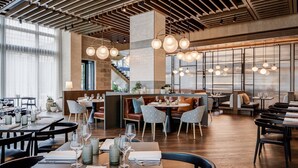 Un interior de restaurante moderno con vigas de madera, lámparas colgantes y una combinación de asientos tipo cabina y mesas.