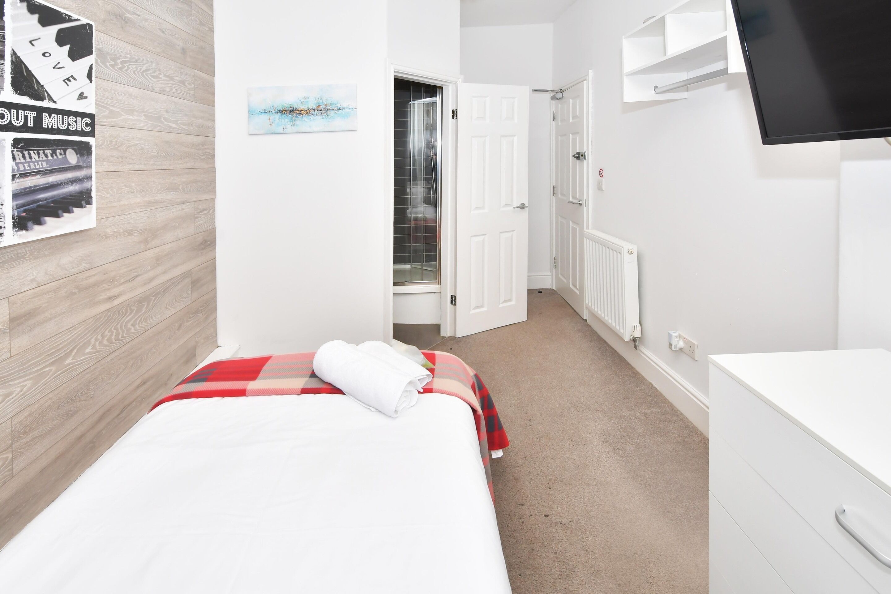 A hotel room with a bed, a white dresser, a TV mounted on the wall, and a door leading to a bathroom.