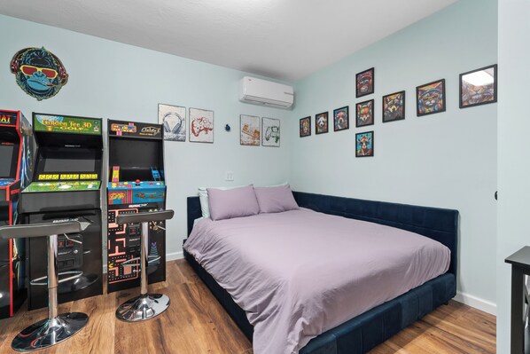 A bedroom with a bed, two arcade machines, and wall art. - That Patio Life (Prescott)
