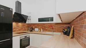 A modern kitchen with a black refrigerator, oven, and microwave, a wooden countertop, a brick backsplash, and a window above the sink.