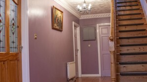 Un pasillo con una escalera de madera, un radiador y una puerta con espejo.