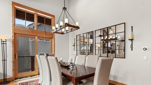 A dining room with a wooden table, white chairs, a chandelier, and a large mirror. - Peak 10 Place - Free Winter Shuttle to Lift - Ski-In, Ski-Out for Experts Only (Breckenridge)