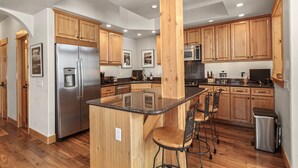 A modern kitchen with wooden cabinets, stainless steel appliances, and a central island with bar stools. - Peak 10 Place - Free Winter Shuttle to Lift - Ski-In, Ski-Out for Experts Only (Breckenridge)