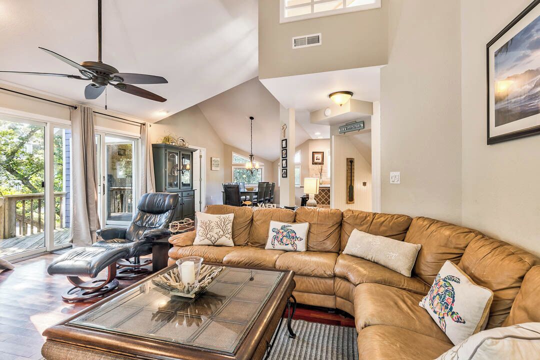 A spacious living room with a leather sectional sofa, a glass coffee table, and a ceiling fan.