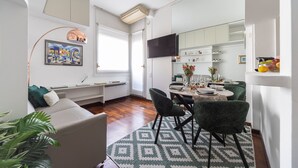 Un salon moderne comprenant un canapé, un coin repas avec des chaises et une table, et une cuisine équipée de placards et d’un téléviseur.