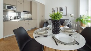 A modern kitchen with a microwave, stove, and sink. There is a dining table set with plates, glasses, and cutlery. A black vase with green plants is on the table. - Fiori - Bright & Stylish loft in the heart of Brera (Milano)