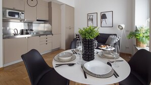 A modern kitchen with a microwave, stove, and sink. There is a dining area with a round table set for two, featuring black and white plates, cutlery, and glasses. A potted plant and framed artwork are on the wall. - Fiori - Bright & Stylish loft in the heart of Brera (Milano)