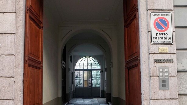 Une entrée d’immeuble avec un panneau indiquant qu’il est interdit de se garer, un portail métallique et une plaque portant l’inscription « Comune di Milano ».