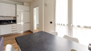 A modern kitchen with white cabinets, a black countertop, and a dining area with a table and chairs. - Candiani Building - Elegant 2-level Apartment with 3 bedroms (Milano)