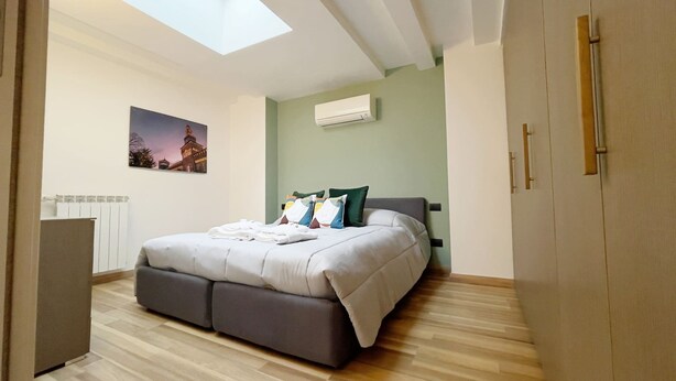 A bedroom with a skylight, a bed with pillows, a radiator, and a picture on the wall. - Candiani Building - Elegant 2-level Apartment with 3 bedroms (Milano)