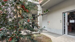 A building entrance with a covered outdoor area, a tree with red berries, and a sign indicating a parking area. - Candiani Building - Elegant 2-level Apartment with 3 bedroms (Milano)